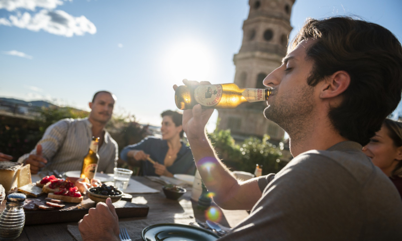 Man drinkt flesje Birra Moretti in de zon